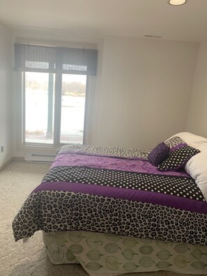 Quarto com cama, janela com persianas e vista para uma paisagem nevada.