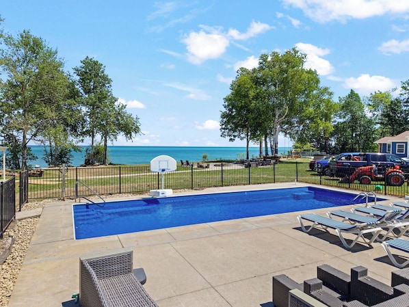 A swimming pool with a basketball hoop, lounge chairs, and a view of the ocean.