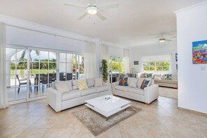 Ein großzügiges Wohnzimmer mit zwei weißen Sofas, einem Couchtisch und einer großen Schiebeglastür, die zu einer Außenpatio führt.