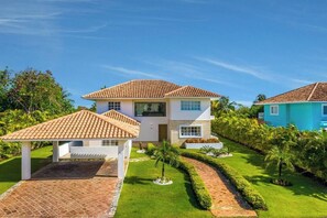 Ein zweistöckiges Haus mit Ziegeldach, einer überdachten Terrasse und einem gepflegten Garten mit Hecken und kleinen Bäumen.