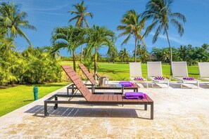 A poolside area with lounge chairs, a table with a drink, and palm trees. - Villa Casa Bonita Punta Cana (Punta Cana)