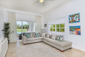 A living room with a beige sectional sofa, a large window, and a ceiling fan. - Villa Casa Bonita Punta Cana (Punta Cana)
