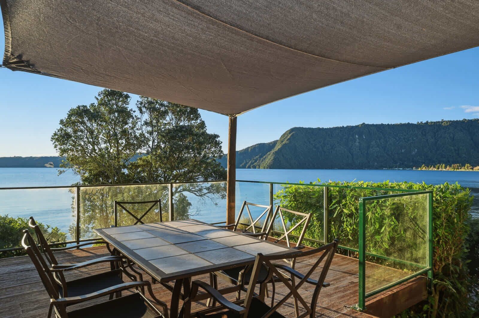 Ein Essbereich im Freien mit Tisch und Stühlen, einer Pergola und Blick auf einen See und Berge.