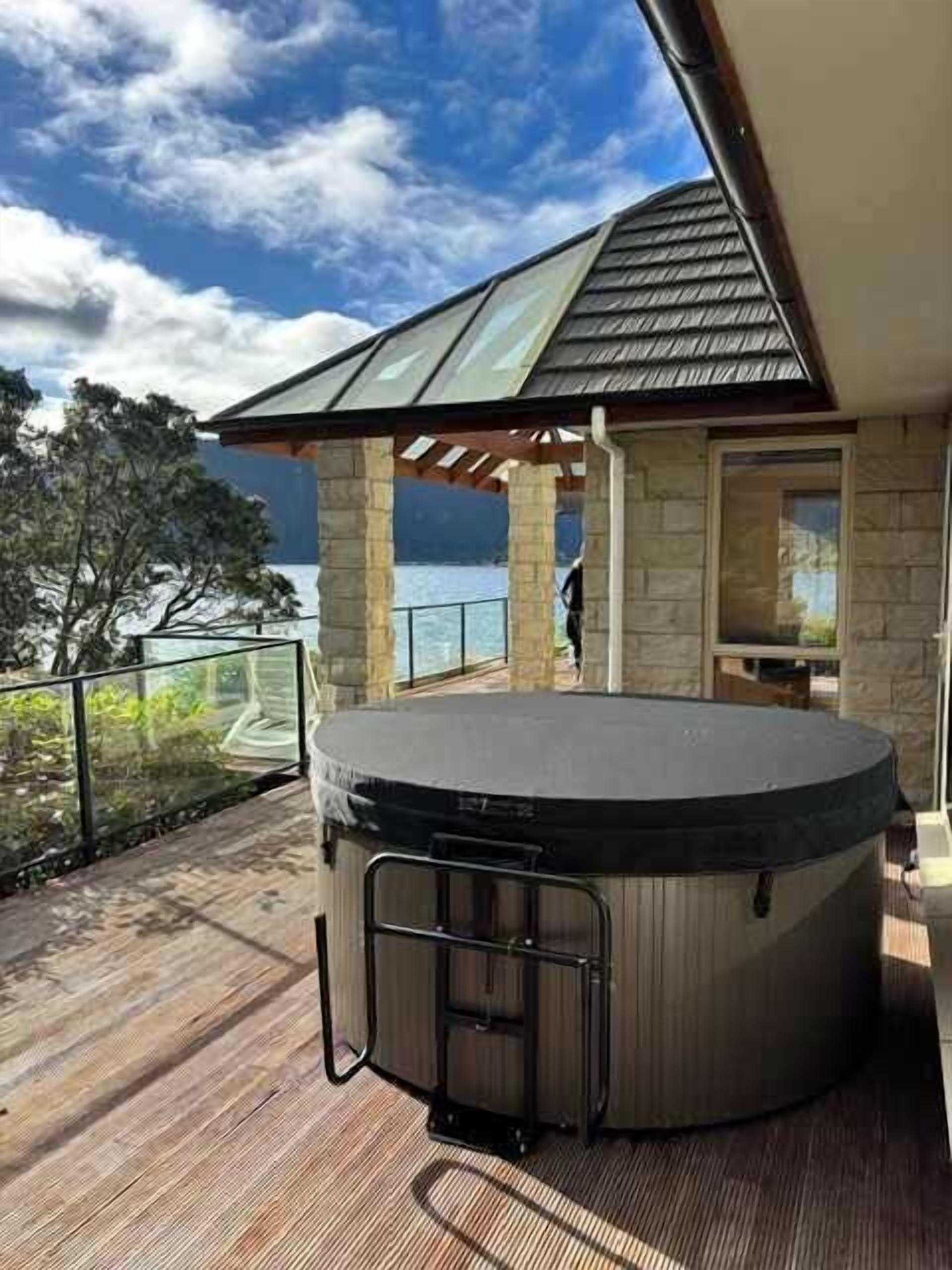 A hot tub on a wooden deck with a stone structure in the background and a view of the sea.