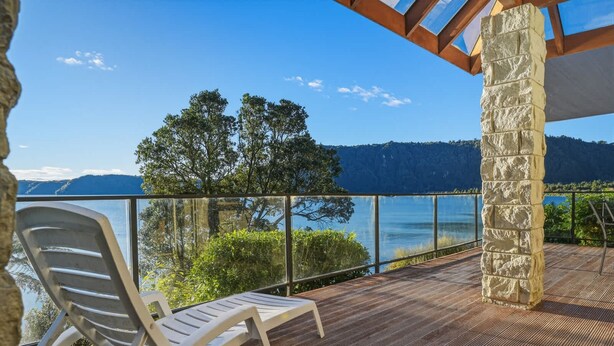 A balcony with a view of a lake and mountains, a stone pillar, and a white chair. - Lion House - Lakefront Spa, Private Beach & Jetty (Rotoiti Forest)