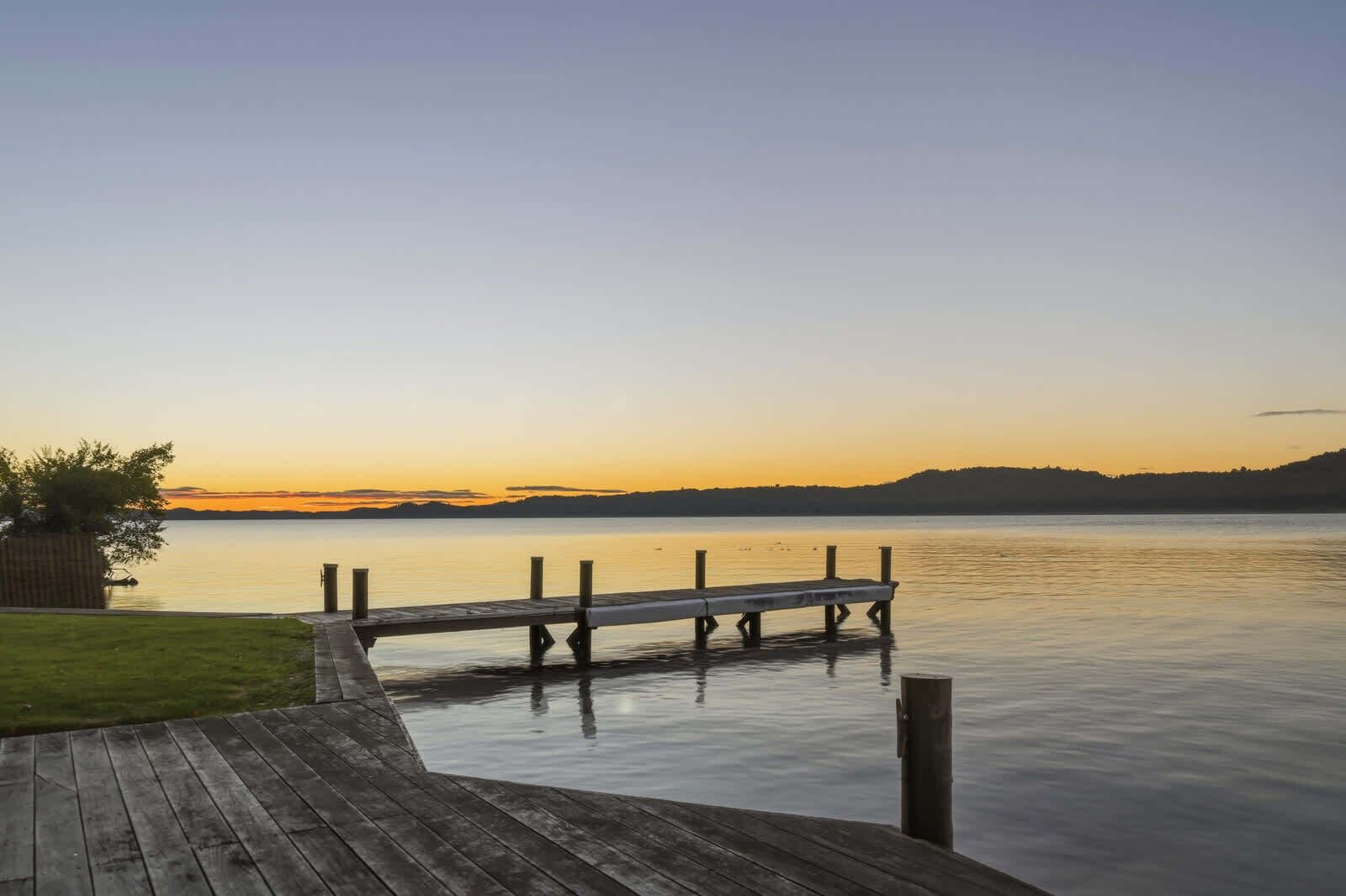 A wooden dock extending into calm water, surrounded by a grassy area and a clear sky.