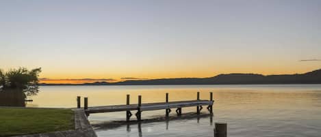 A wooden dock extending into calm water, surrounded by a grassy area and a clear sky.