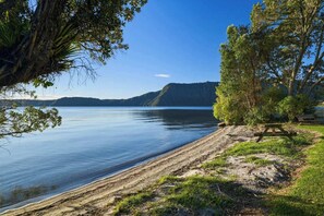 A lakeside view with a picnic table, trees, and a distant mountain range. - The Lion House - Rotoiti Lakefront, Beach & Jetty (Rotoiti Forest)