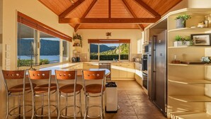 A modern kitchen with a wooden ceiling, large windows, and a view of the outdoors. - Lion House - Lakefront Spa, Private Beach & Jetty (Rotoiti Forest)