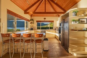 A modern kitchen with a wooden ceiling, large windows, and a view of the outdoors. - The Lion House - Rotoiti Lakefront, Beach & Jetty (Rotoiti Forest)