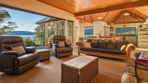 A spacious living area with leather sofas, a dining table, and a view of a lake. - Lion House - Lakefront Spa, Private Beach & Jetty (Rotoiti Forest)