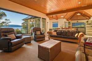 A spacious living area with leather sofas, a dining table, and a view of a lake. - The Lion House - Rotoiti Lakefront, Beach & Jetty (Rotoiti Forest)