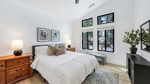 Ein Schlafzimmer mit einem Bett, zwei Nachttischen, einem Fenster und einer Zimmerpflanze.