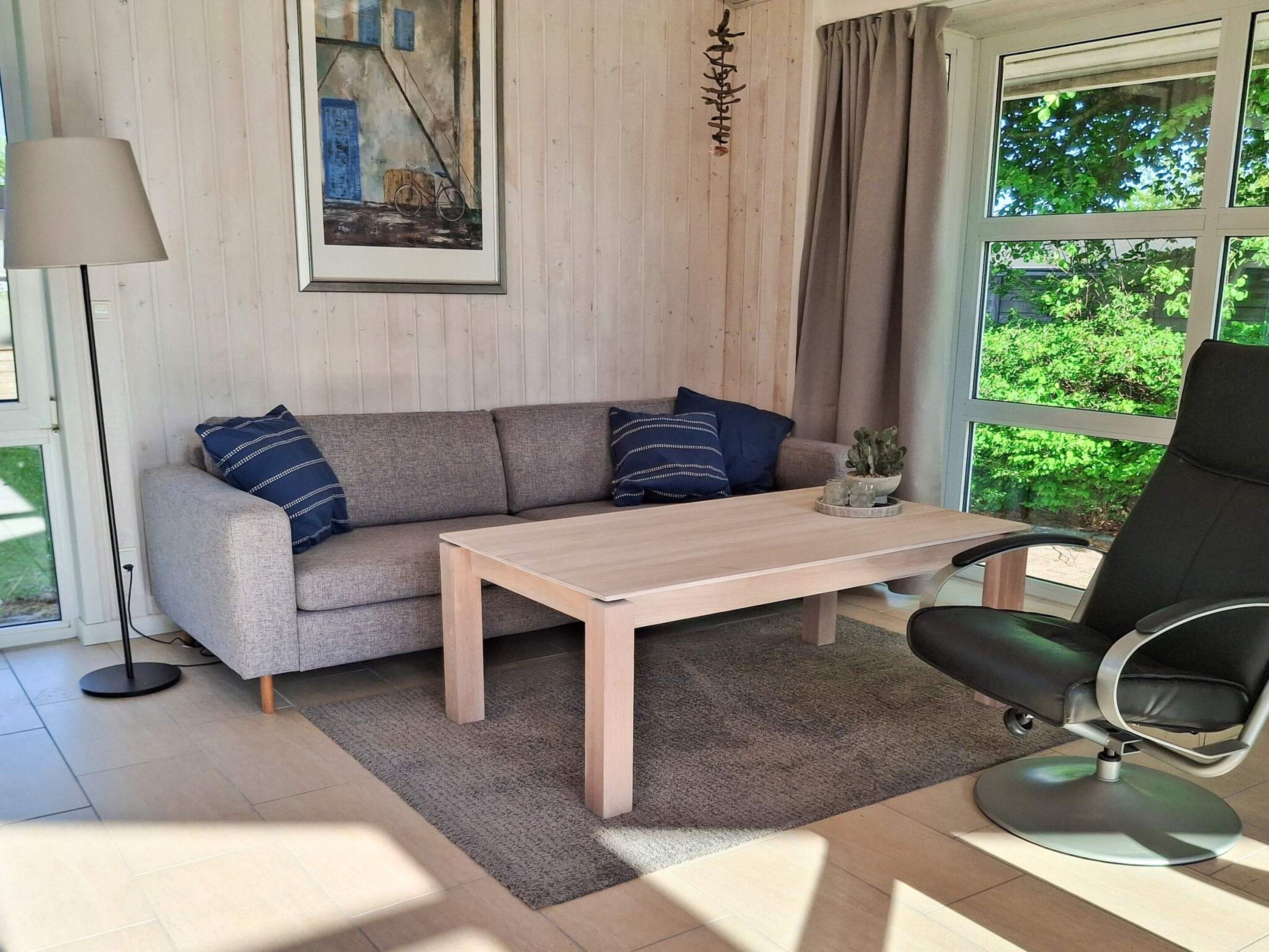 A living room with a sofa, a coffee table, a chair, a lamp, a painting, and a window with a view of greenery.