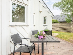 An outdoor seating area with a table and chairs, a flower arrangement, and a view of a white building with windows. - 5 Star Holiday Home in Odder (Odder)