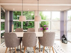 A dining area with a table and chairs, large windows, and a view of greenery outside. - 5 Star Holiday Home in Odder (Odder)