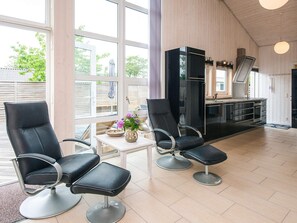 A modern interior with two black leather chairs, a small table with a vase, and a kitchen area with a refrigerator and oven. - 5 Star Holiday Home in Odder (Odder)