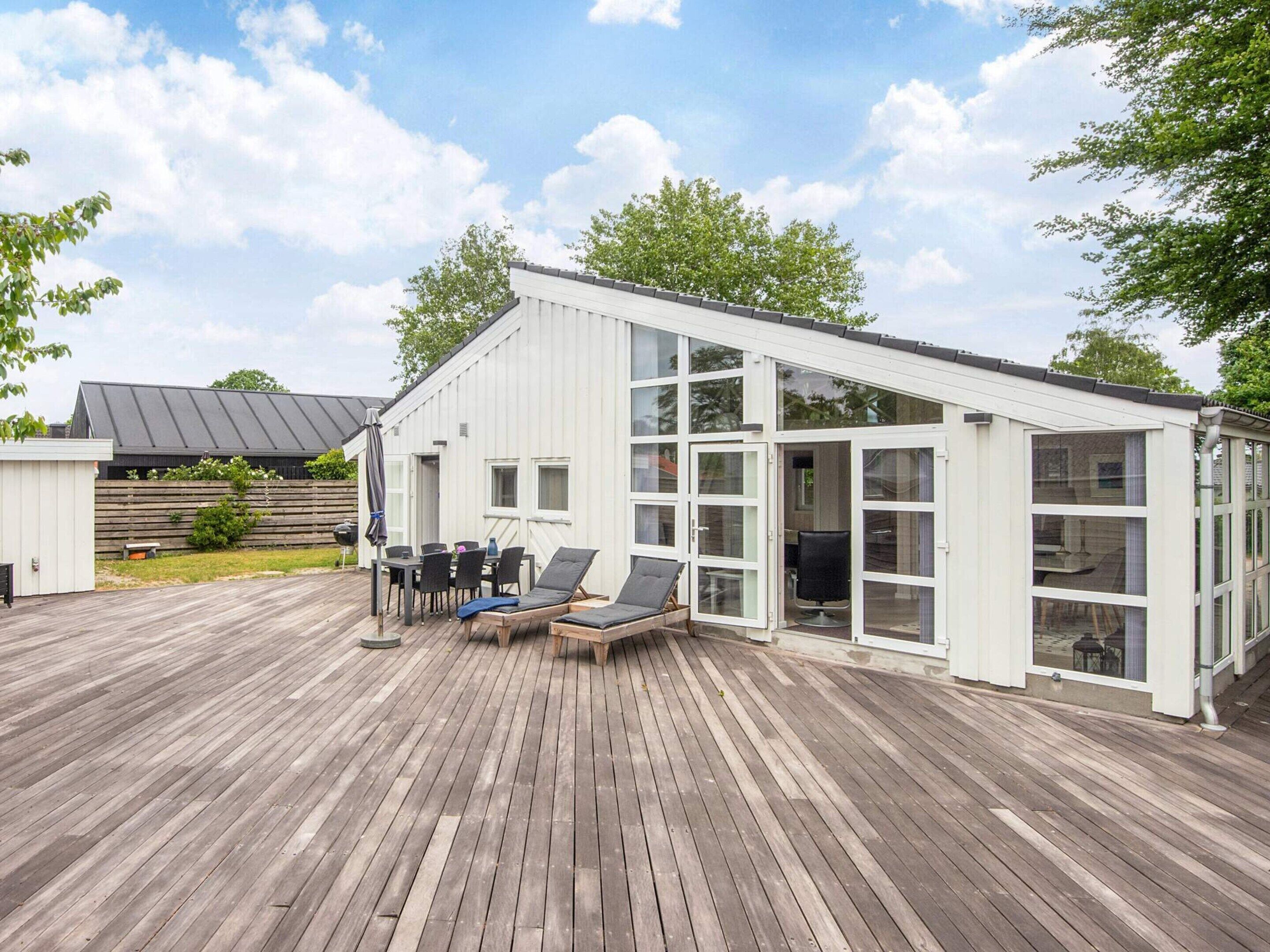 A modern building with a deck, a covered seating area, and a glass enclosure.