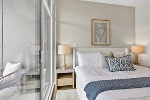 A bedroom with a bed, two bedside lamps, a framed picture, and a glass door leading to a balcony.