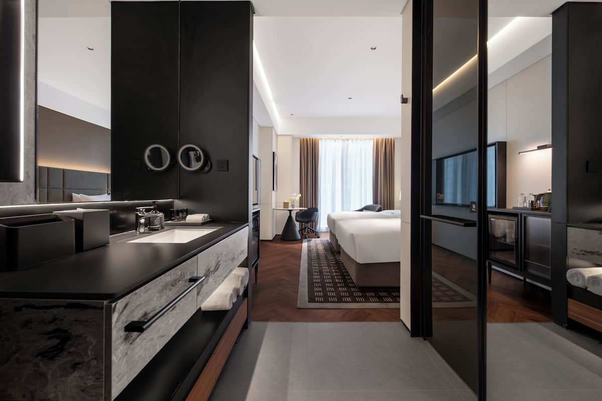 Una habitación de hotel moderna con una cama grande, un baño independiente con tocador, televisión y vistas a la ciudad.