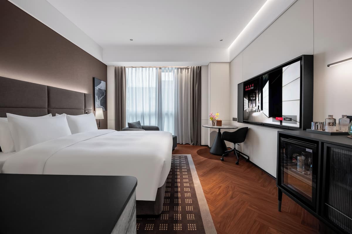 Una habitación de hotel con una cama grande, un escritorio, una silla, un televisor y un minibar.