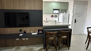 A modern kitchen with a built-in TV, a dining area with two chairs, and a white refrigerator. - Casa Confortavel em Foz do Iguaçu (Foz do Iguaçu)