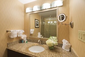 Un baño de hotel con encimera de granito, lavamanos, espejo y toallero.