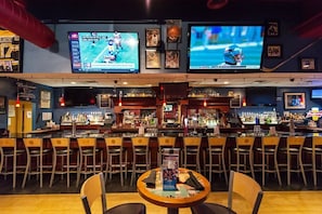 A bar area with multiple TVs displaying sports, a bar counter with bottles, and several bar stools.