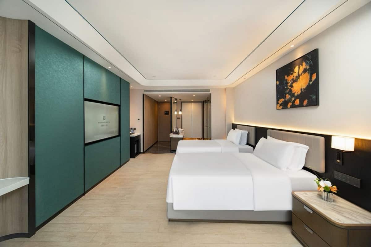 A hotel room with a bed, bedside tables, a TV, and a painting on the wall.