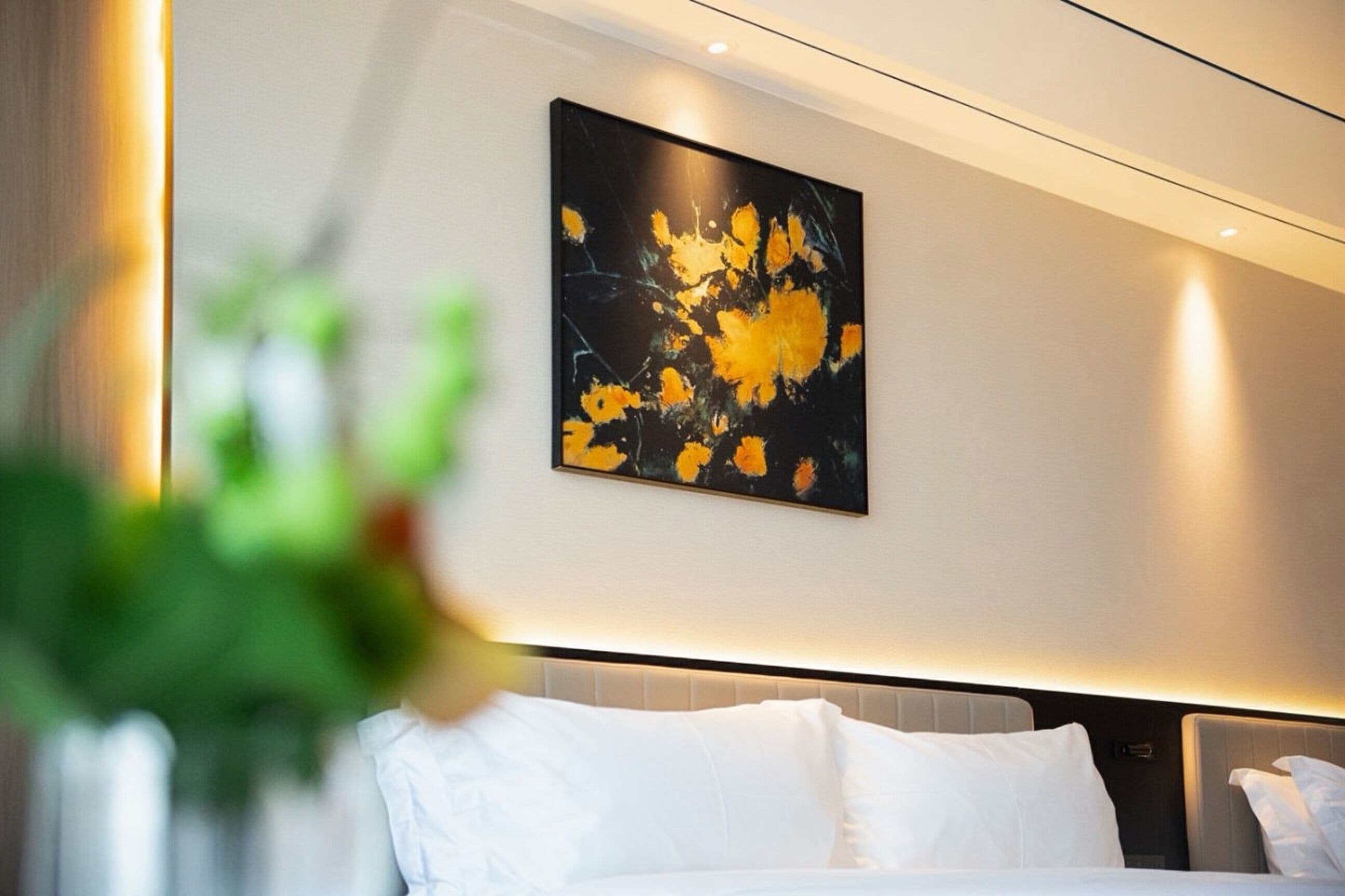 Una habitación de hotel moderna con una cama grande, cabecero con iluminación integrada y un cuadro abstracto colgado en la pared.