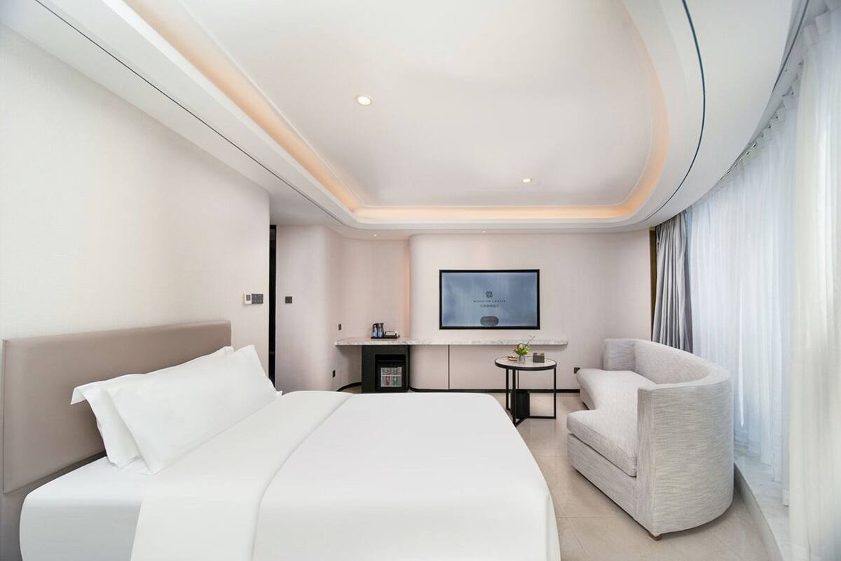 A modern hotel room with a large bed, a seating area, a flat-screen TV, and a small table.