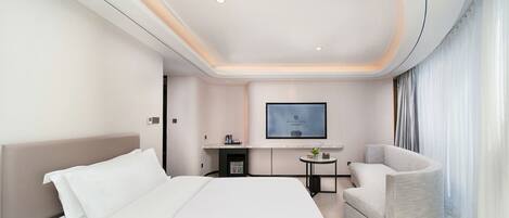 Ein modernes Hotelzimmer mit einem großen Bett, einer Sitzecke, einem Flachbildfernseher und einem kleinen Tisch.