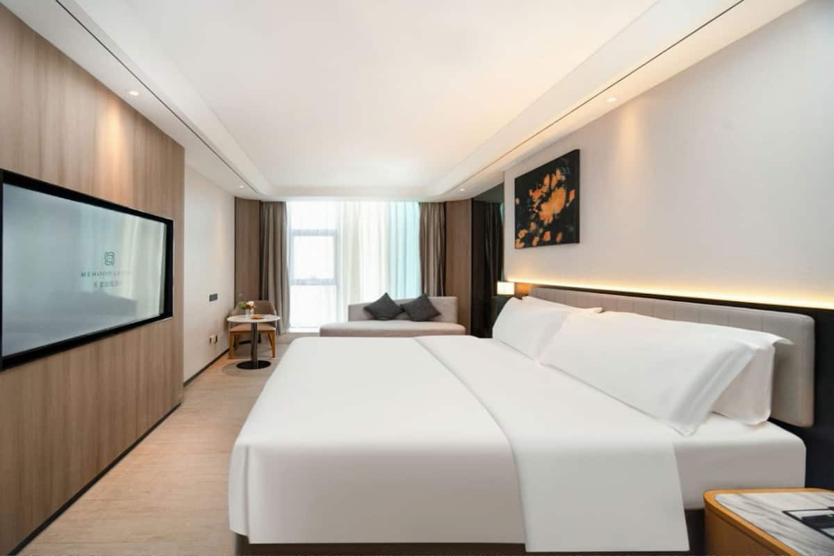 A modern hotel room with a large bed, a TV mounted on the wall, and a view of the city through the window.