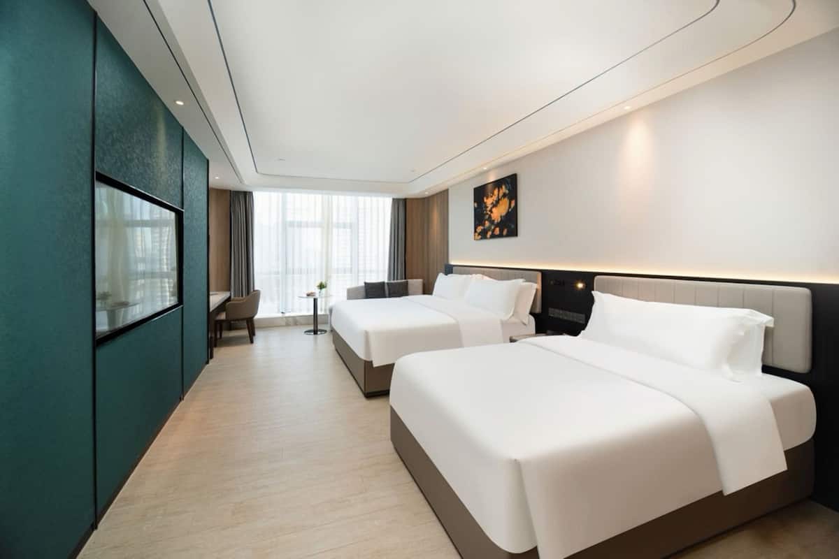 A hotel room with two beds, a TV, a desk, and a window with curtains.