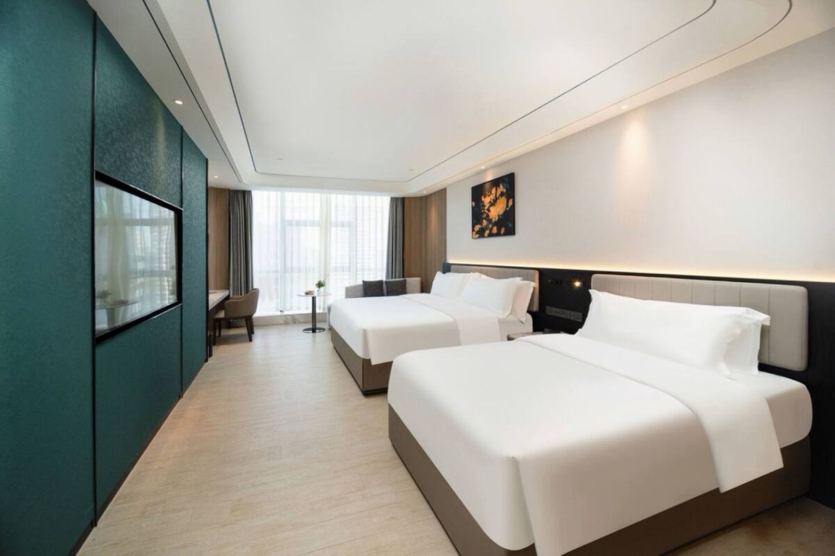 Quarto de hotel com duas camas, televisão, escrivaninha e janela com cortinas.