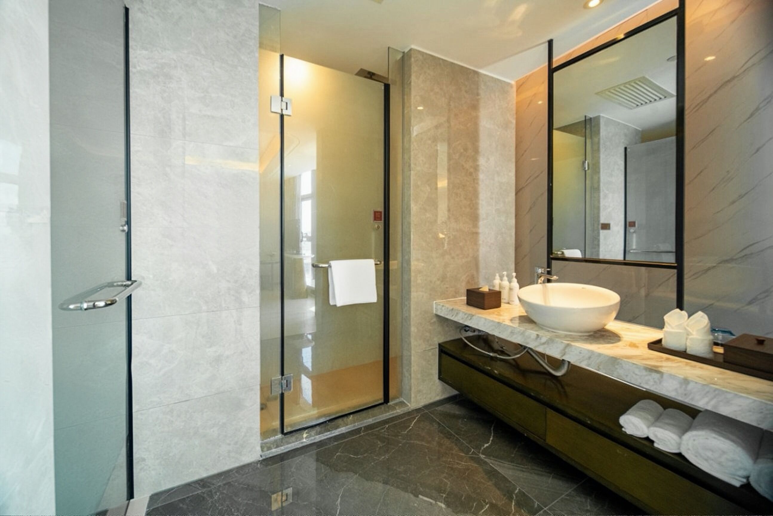 A modern bathroom with a glass shower enclosure, a marble vanity, and a large mirror.