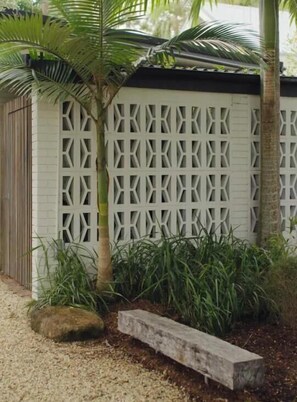 Eine weiße Wand mit einem geometrischen Gittermuster, eine Palme und eine Steinsitzbank.