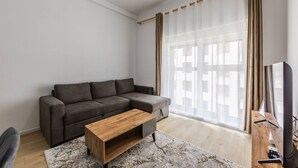 Un soggiorno con un divano grigio, un tavolino in legno, una televisione e tende leggere.