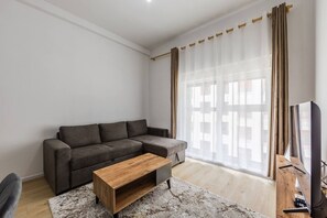 A living room with a grey sofa, a wooden coffee table, a TV, and sheer curtains. - Central Quiet Tirana Flat 1BR Apartment (Tirana)