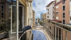 A balcony with a chair, a glass door, and a view of a street with parked cars and buildings. - Sunset Apartment 1BR Escape (Durrës)