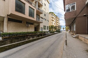 A street with multi-story buildings, a sidewalk, and a median with plants. - Sunset Apartment 1BR Escape (Durrës)