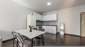A compact kitchen with white cabinets, a dining table with chairs, and a small refrigerator. - Sunset Apartment 1BR Escape (Durrës)