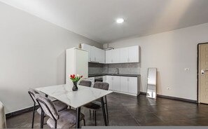 A compact kitchen with white cabinets, a dining table with chairs, and a small refrigerator. - Sunset Apartment 1BR Escape (Durrës)