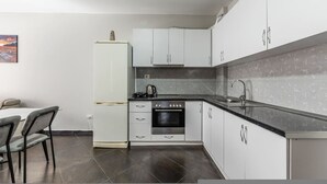 A compact kitchen with white cabinets, a black countertop, a built-in oven, and a refrigerator. - Sunset Apartment 1BR Escape (Durrës)