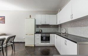 A compact kitchen with white cabinets, a black countertop, a built-in oven, and a refrigerator. - Sunset Apartment 1BR Escape (Durrës)