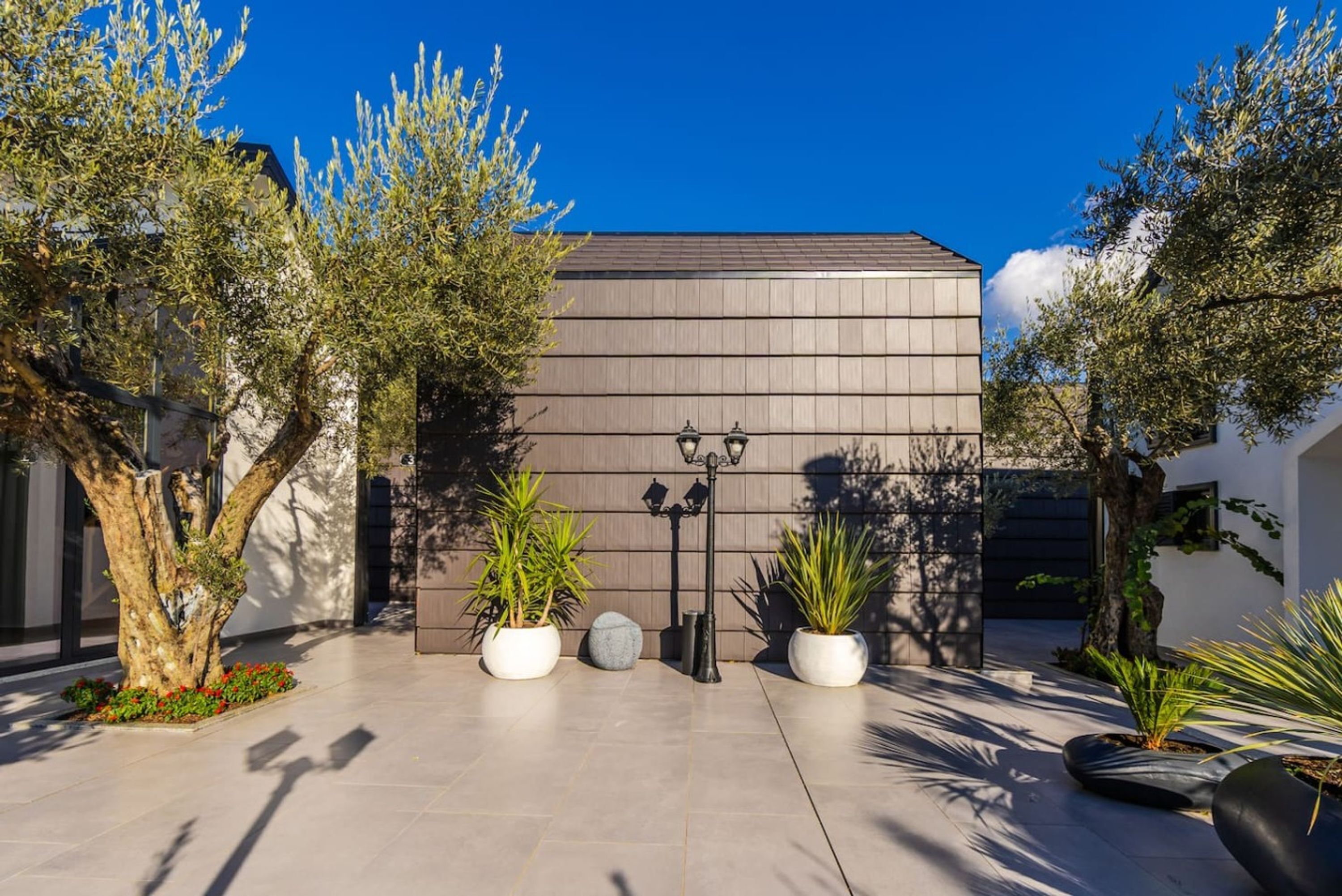 A modern building with a flat roof, surrounded by potted plants and trees.