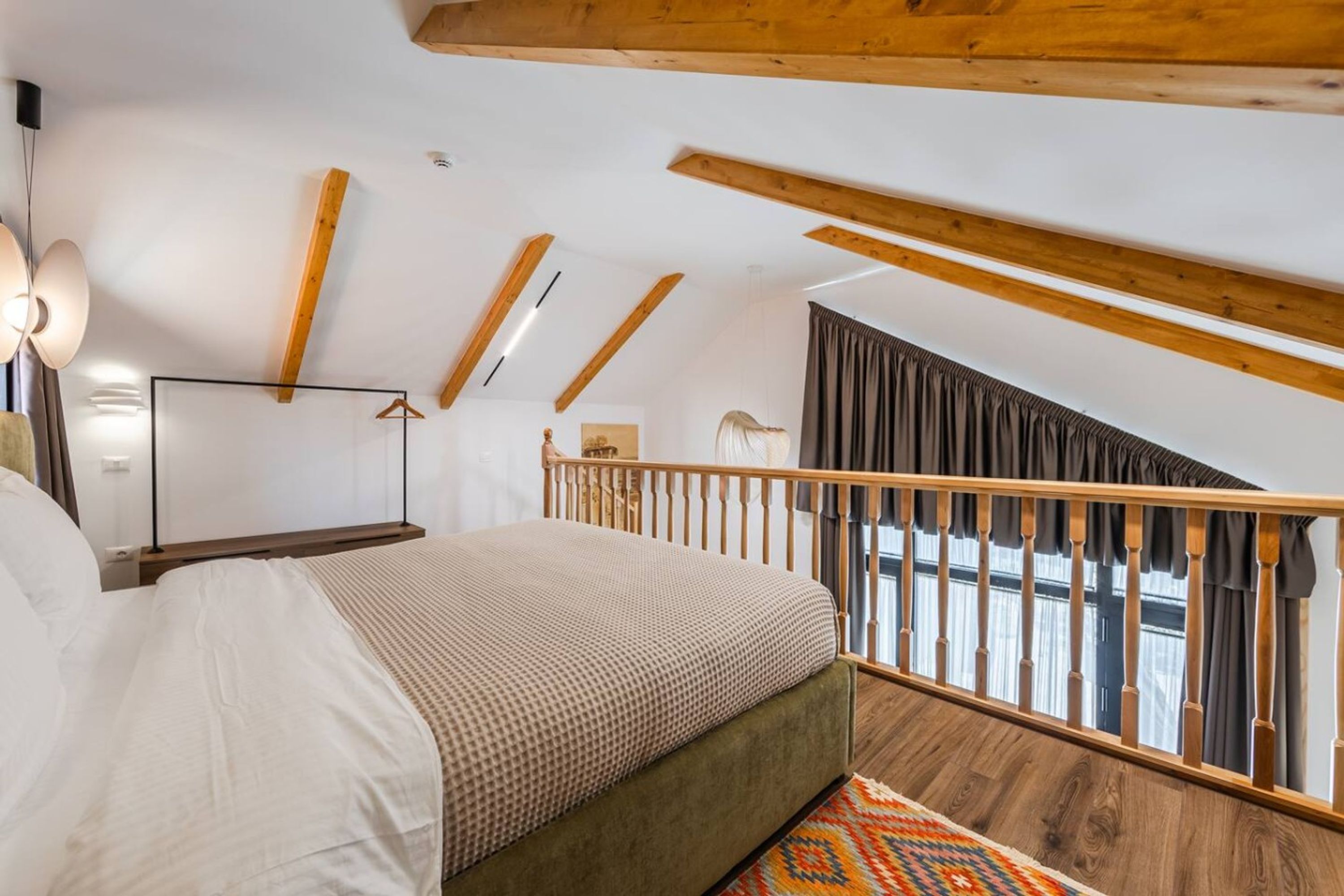 A bedroom with a bed, a wooden ceiling, a staircase, and a view of the outside.