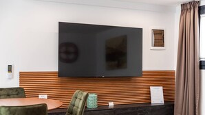 A modern hotel lobby with a large flat-screen TV mounted on the wall, a reception desk, and a seating area with chairs and a small table. - Muraga Villas 7 Kupola (Dajt)