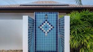 A blue-tiled shower enclosure with a central design, surrounded by white walls, and a palm plant to the right. - Orchid Paradise Homes OPV307 (Tambon Hin Lek Fai)