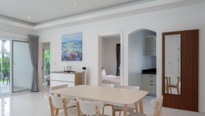A modern dining area with a white table and chairs, a painting on the wall, and a view of the outdoors. - Orchid Paradise Homes OPV307 (Tambon Hin Lek Fai)
